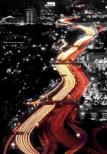 A shot of taillights flowing through a cityscape. It looks like a river of light. The photographer has added a black-and-white effect to the city scape meaning the only color is the light from the traffic