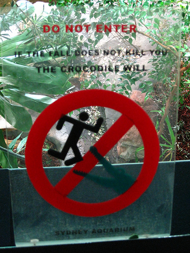 A "No Entry" sign that's be adapted to show a man being dragged off by a crocodile. The sign reads "DO NOT ENTER - If the fall does not kill you the crocodile will."