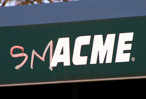 A professional sign reading "ACME" which has been graffitied with SM - reading (phonetically) Smack Me!