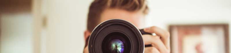 A photograph of a man holding a camera. You can't see his face but the camera lens is very prominent.